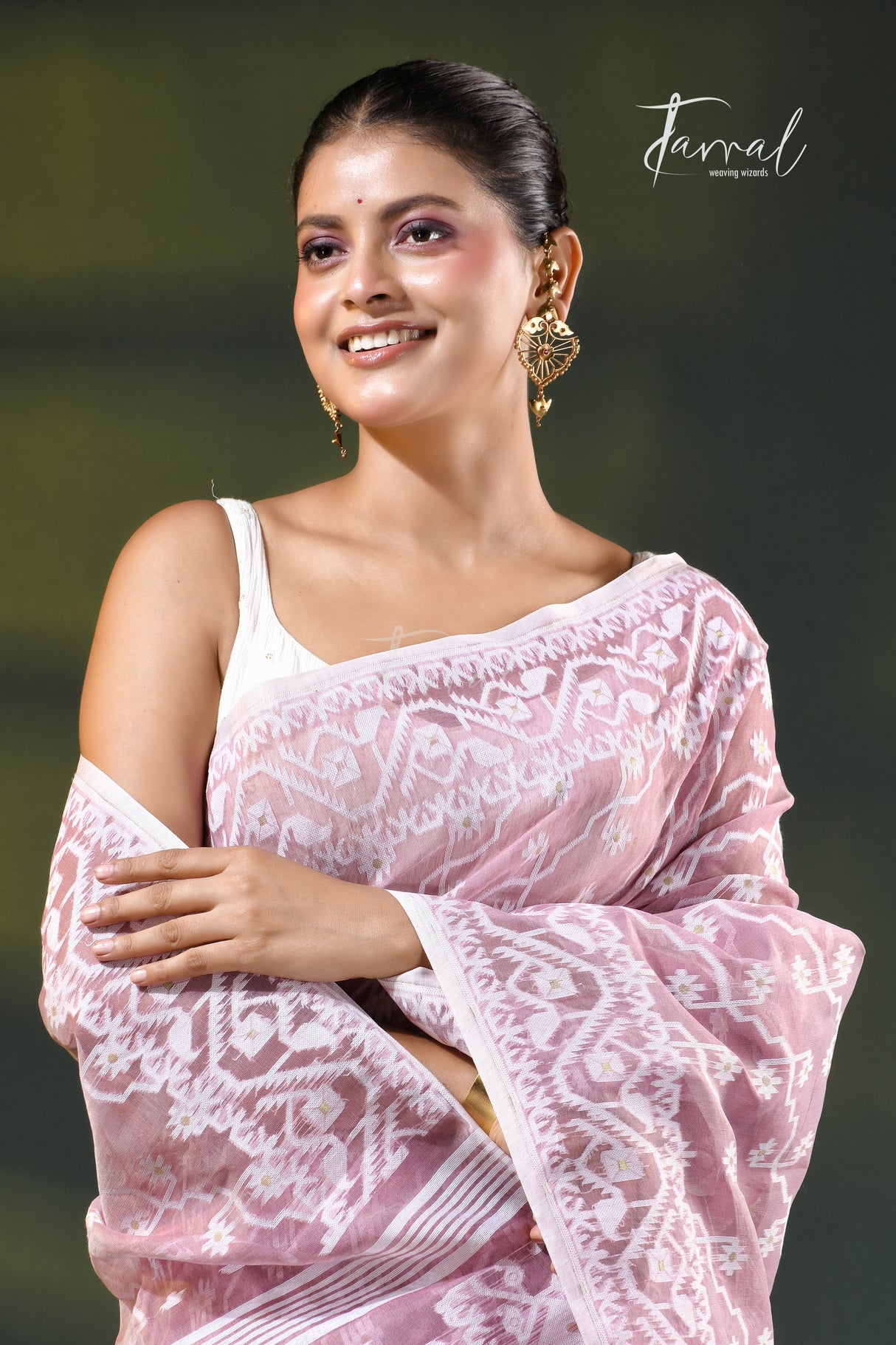 A woman modeling a onion pink and white patterned saree with a white blouse, accessorized with gold earrings, against a dark green gradient background. The brand name 'Farral' is visible in the top right corner.