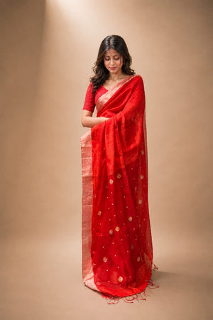 Woman wearing a red saree with gold patterns on a beige background