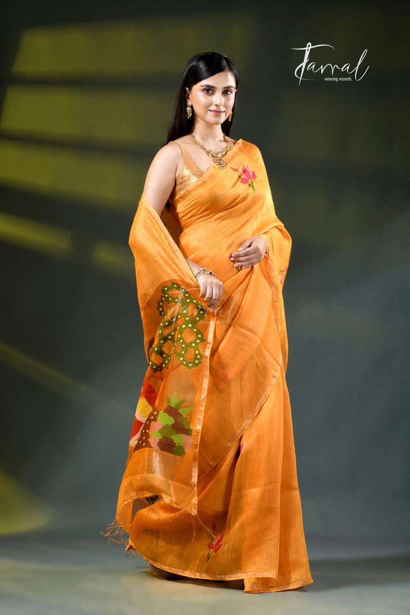 A woman modeling an orange saree with green and yellow floral embroidery, standing against a dark gray studio background with yellow lighting. The brand name 'Jarral' is visible in the top right corner.