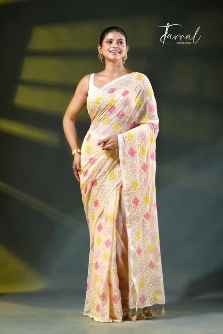 A woman modeling a light beige saree with pink and yellow floral patterns, standing on a dark stage with a 'Farral' watermark in the upper right.