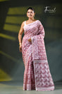 A woman modeling a onion pink and white patterned saree with a white blouse, accessorized with gold earrings, against a dark green gradient background. The brand name 'Farral' is visible in the top right corner.