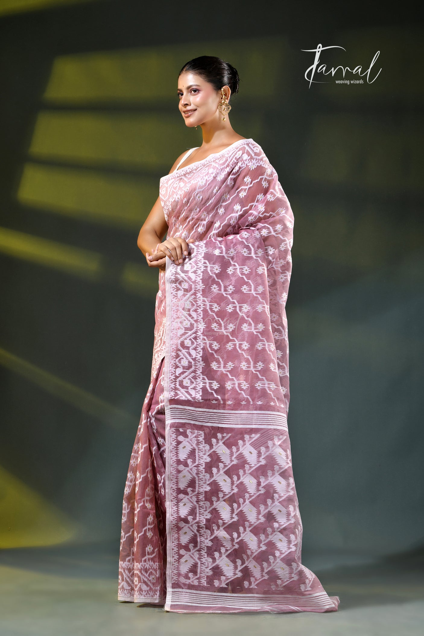 A woman modeling a onion pink and white patterned saree with a white blouse, accessorized with gold earrings, against a dark green gradient background. The brand name 'Farral' is visible in the top right corner.