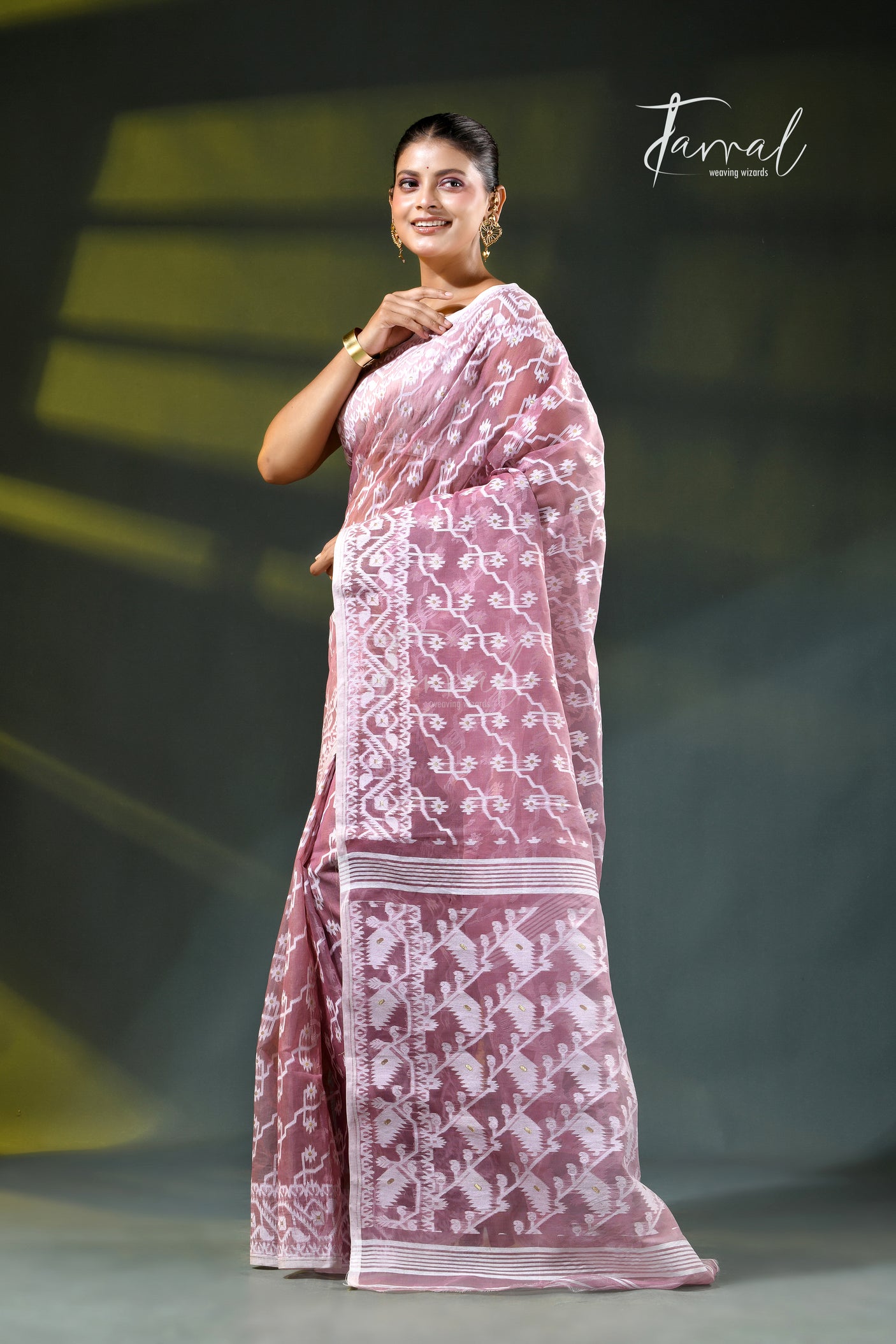A woman modeling a onion pink and white patterned saree with a white blouse, accessorized with gold earrings, against a dark green gradient background. The brand name 'Farral' is visible in the top right corner.