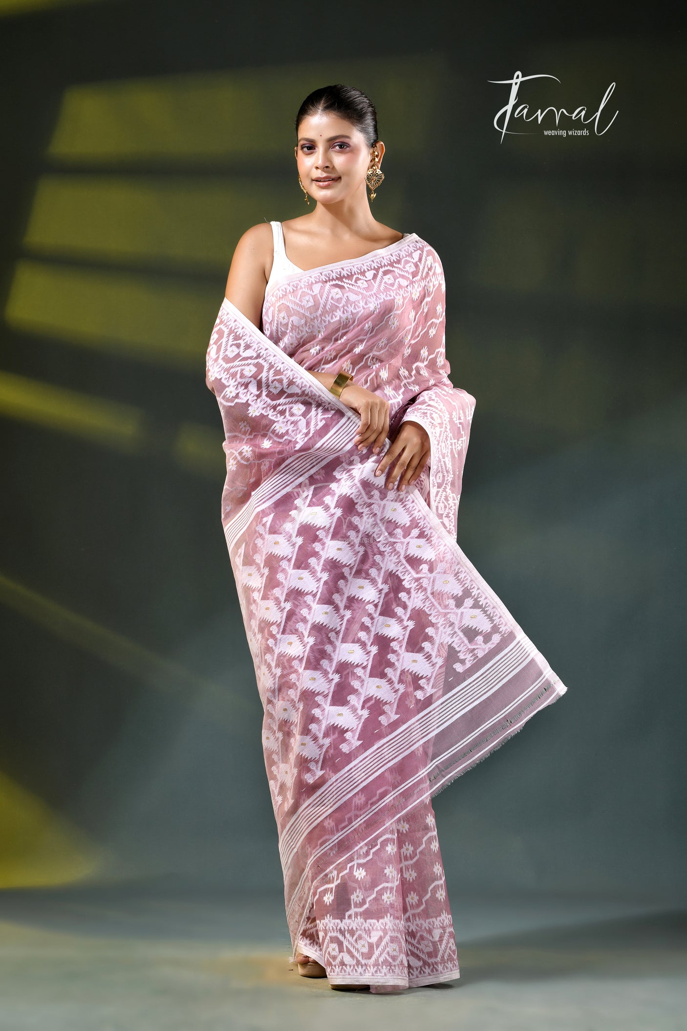 A woman modeling a onion pink and white patterned saree with a white blouse, accessorized with gold earrings, against a dark green gradient background. The brand name 'Farral' is visible in the top right corner.