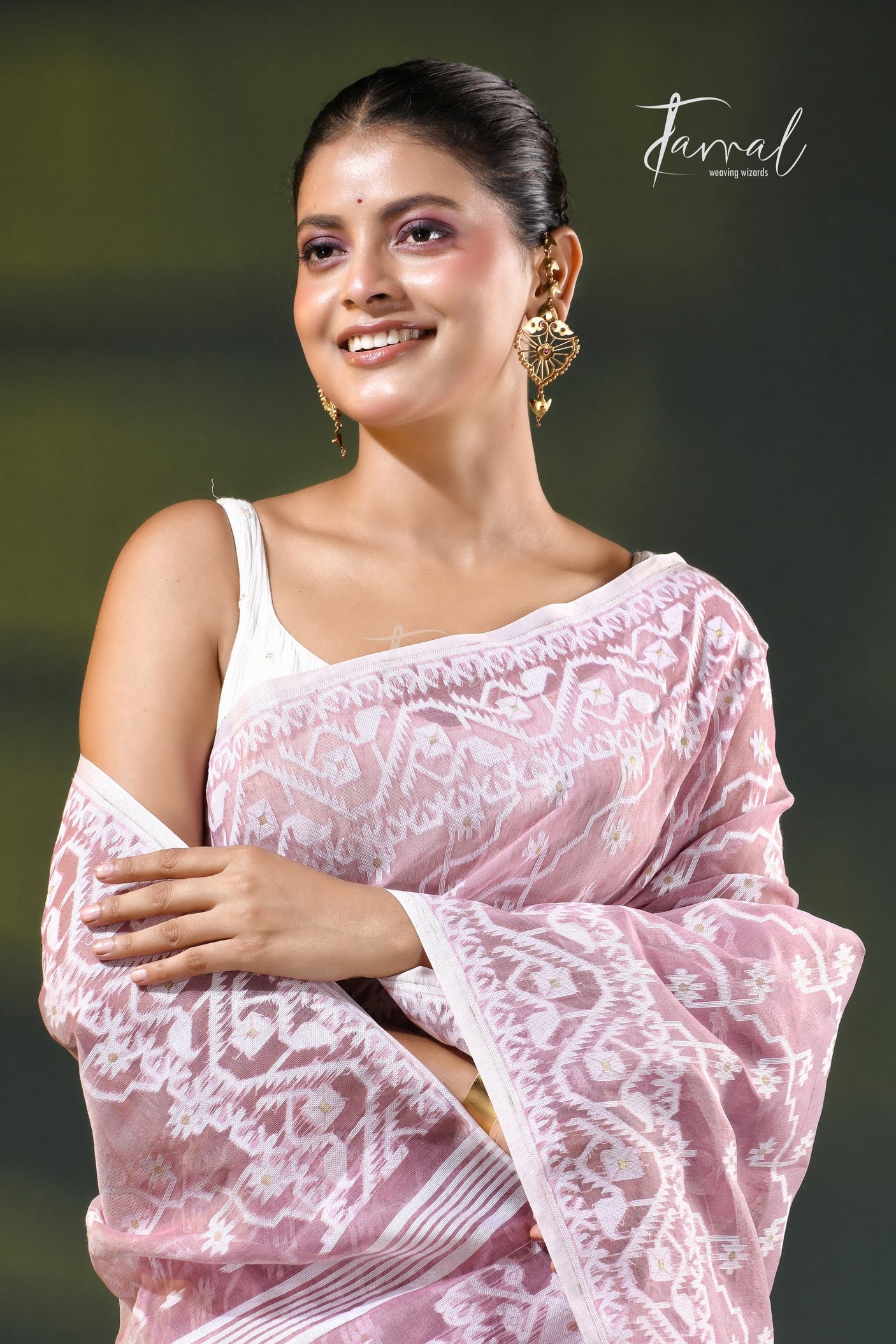 A woman modeling a onion pink and white patterned saree with a white blouse, accessorized with gold earrings, against a dark green gradient background. The brand name 'Farral' is visible in the top right corner.