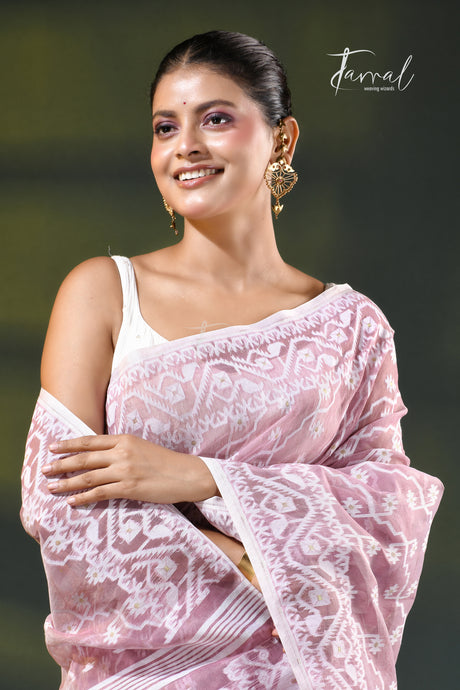 A woman modeling a onion pink and white patterned saree with a white blouse, accessorized with gold earrings, against a dark green gradient background. The brand name 'Farral' is visible in the top right corner.