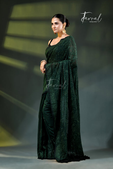 A model wearing a dark forest green embroidered saree with a matching dupatta, standing on a runway under stage lighting. The brand name 'Farral' is visible as a watermark and logo.