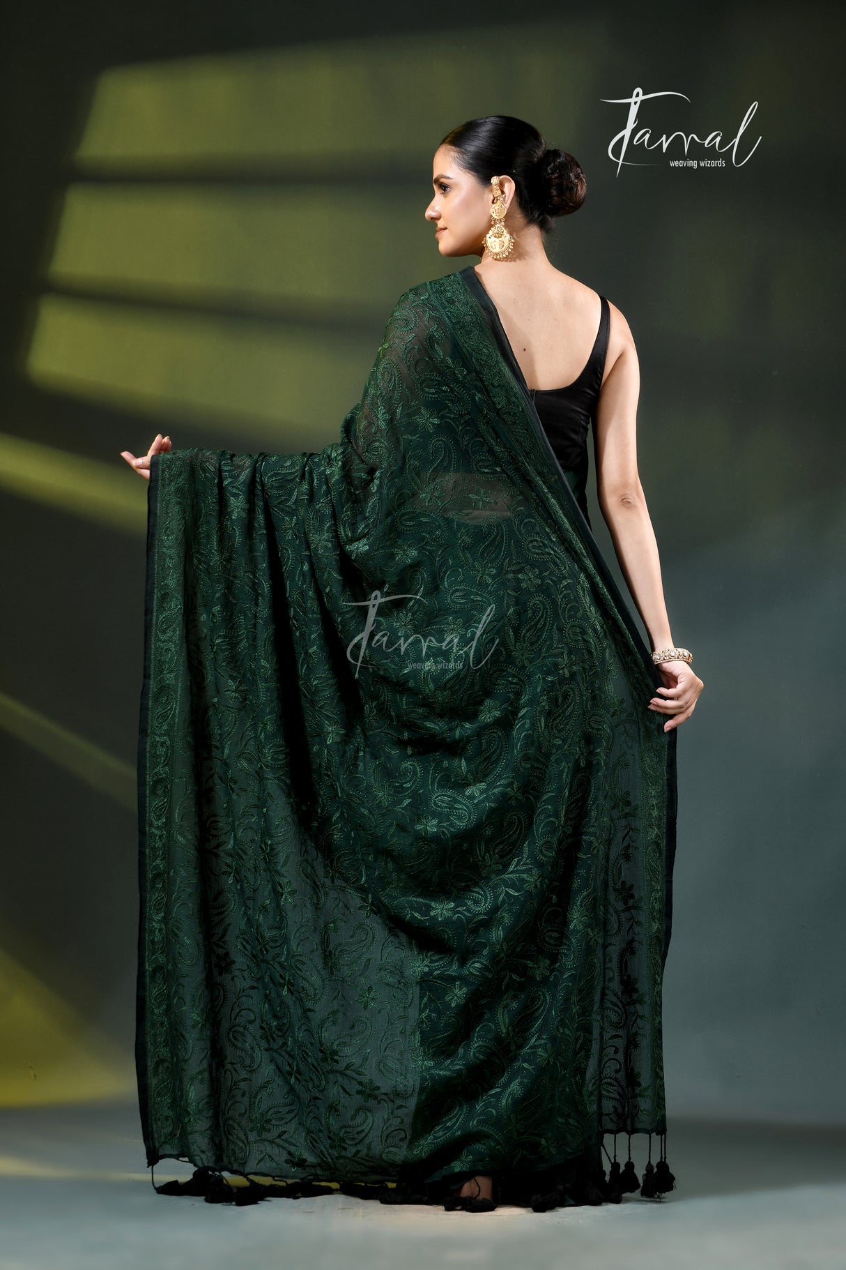 A model wearing a dark forest green embroidered saree with a black sleeveless top, standing on a runway under spotlighting. The brand name 'Farral' is visible as a watermark and logo.