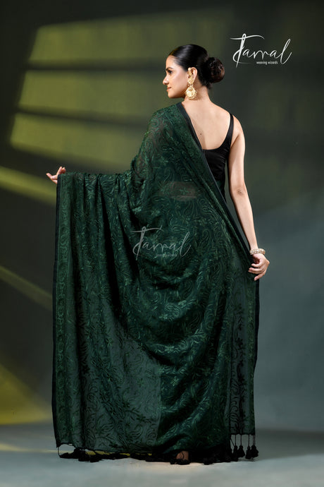 A model wearing a dark forest green embroidered saree with a black sleeveless top, standing on a runway under spotlighting. The brand name 'Farral' is visible as a watermark and logo.